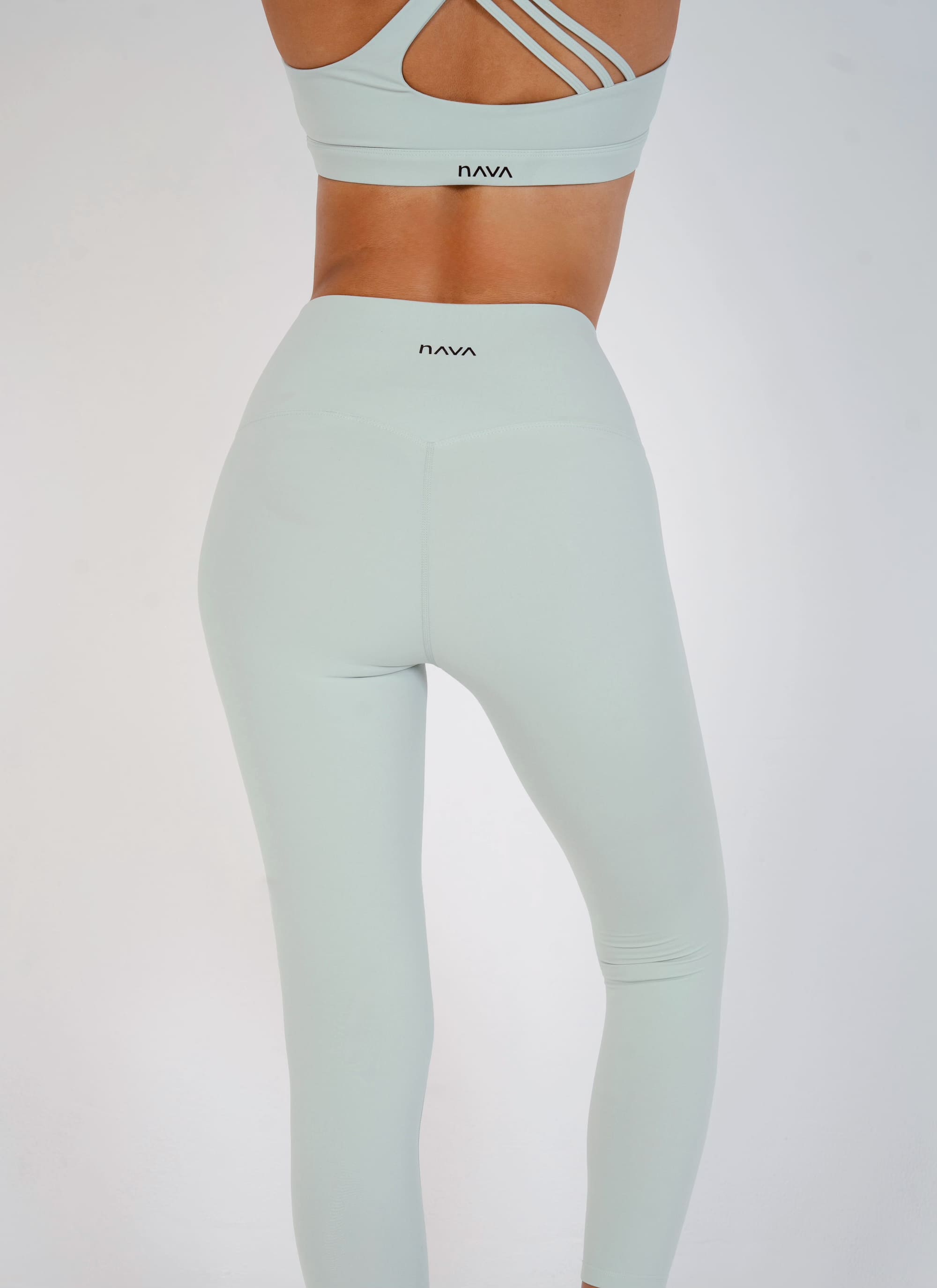 Person wearing light gray leggings and sports bra with 'RAVA' branding on a white background