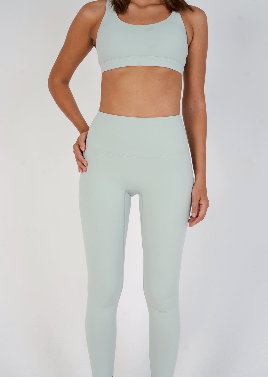 Person wearing a light green sports bra and leggings set on a white background