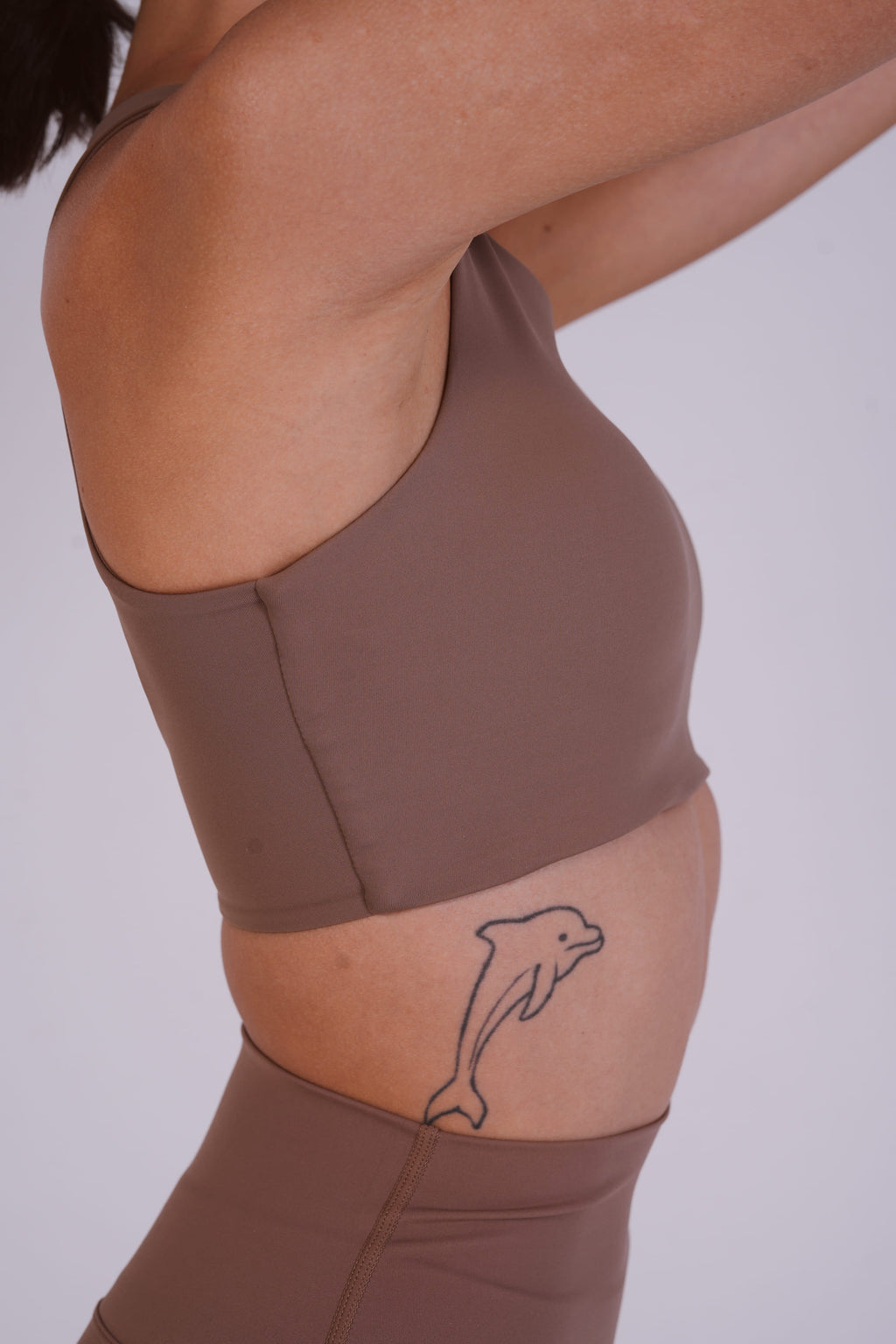 Person wearing a brown athletic outfit with a dolphin tattoo on a plain background