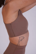 Person wearing a brown athletic outfit with a dolphin tattoo on a plain background