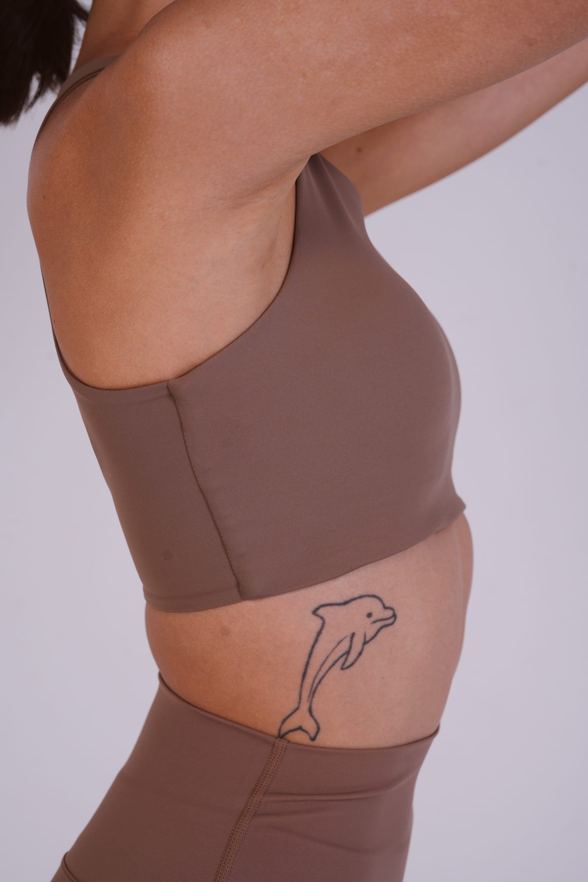Person wearing a brown athletic outfit with a dolphin tattoo on a plain background