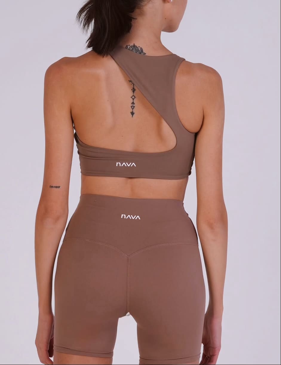 Woman wearing a brown sports bra and shorts set with 'NAVA' branding on a light gray background