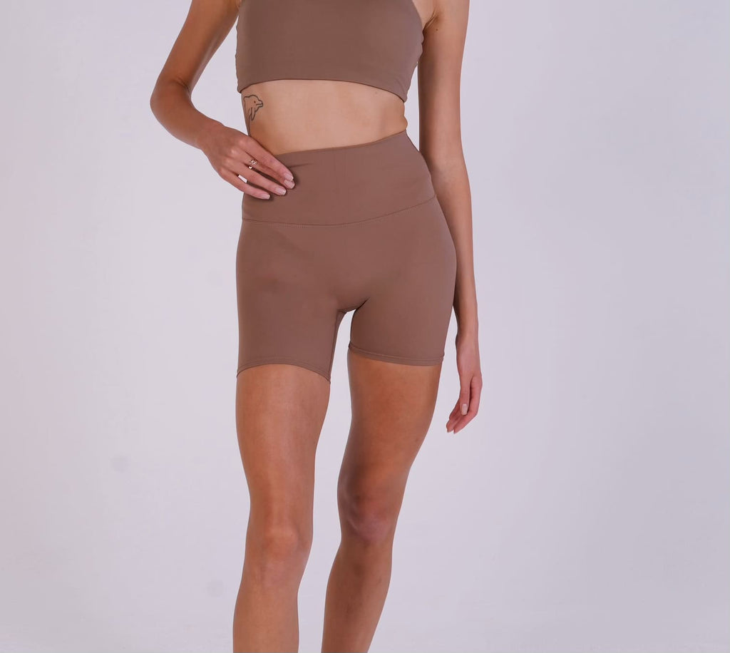 Woman wearing brown athletic shorts and top on a white background