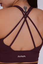 Burgundy sports bra with criss-cross straps and 'Nava' branding on a white background