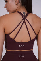 Woman wearing a maroon sports bra and leggings with 'NAVA' branding on a plain background