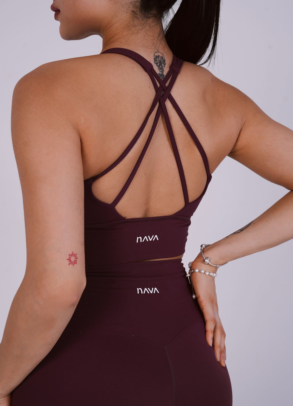Person wearing a maroon sports bra and leggings with 'NAVA' branding on a plain background