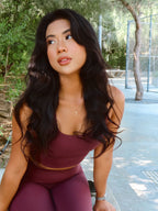 Woman in maroon athletic wear sitting outdoors with trees in the background