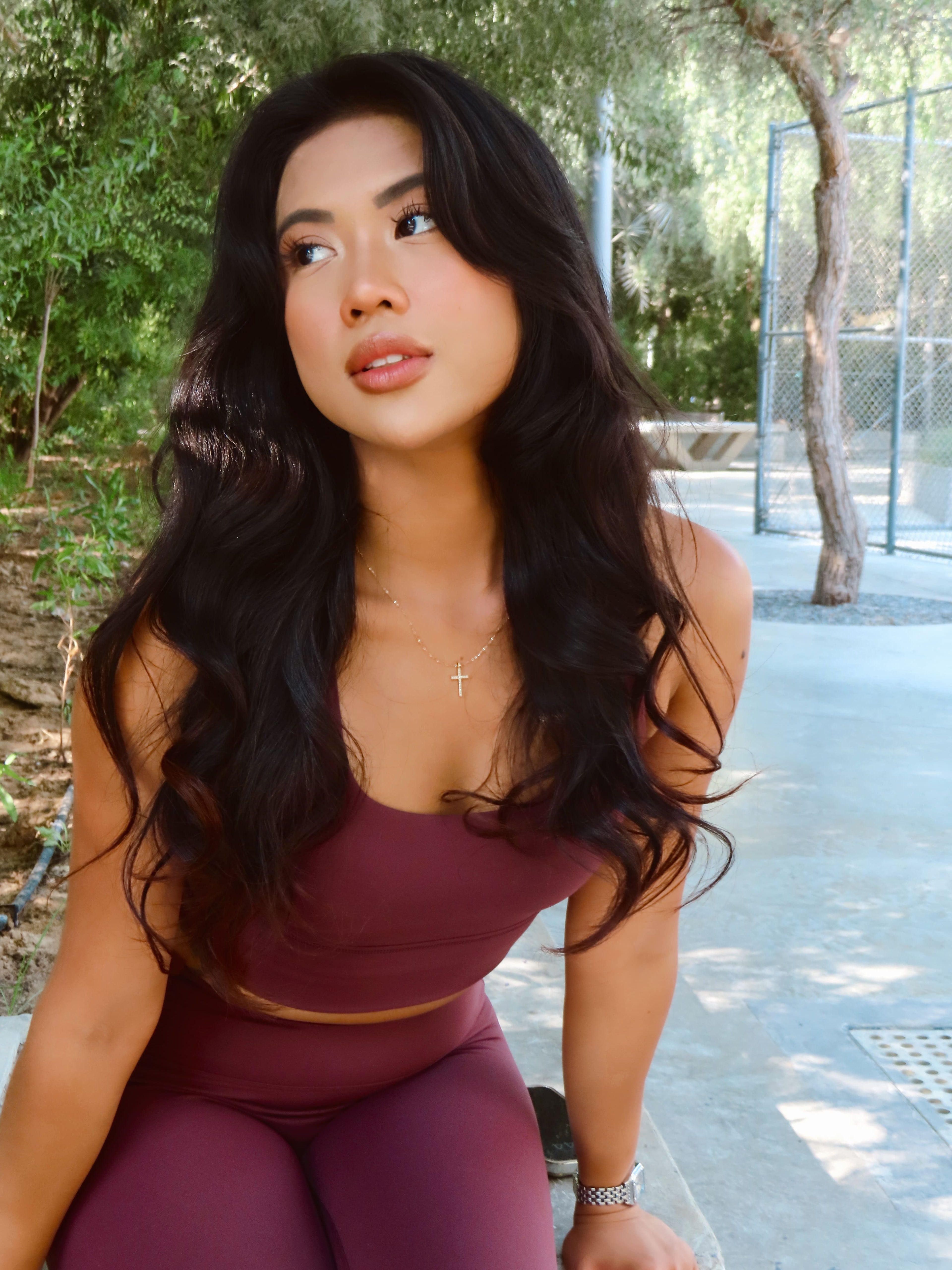 Woman in maroon athletic wear sitting outdoors with trees in the background