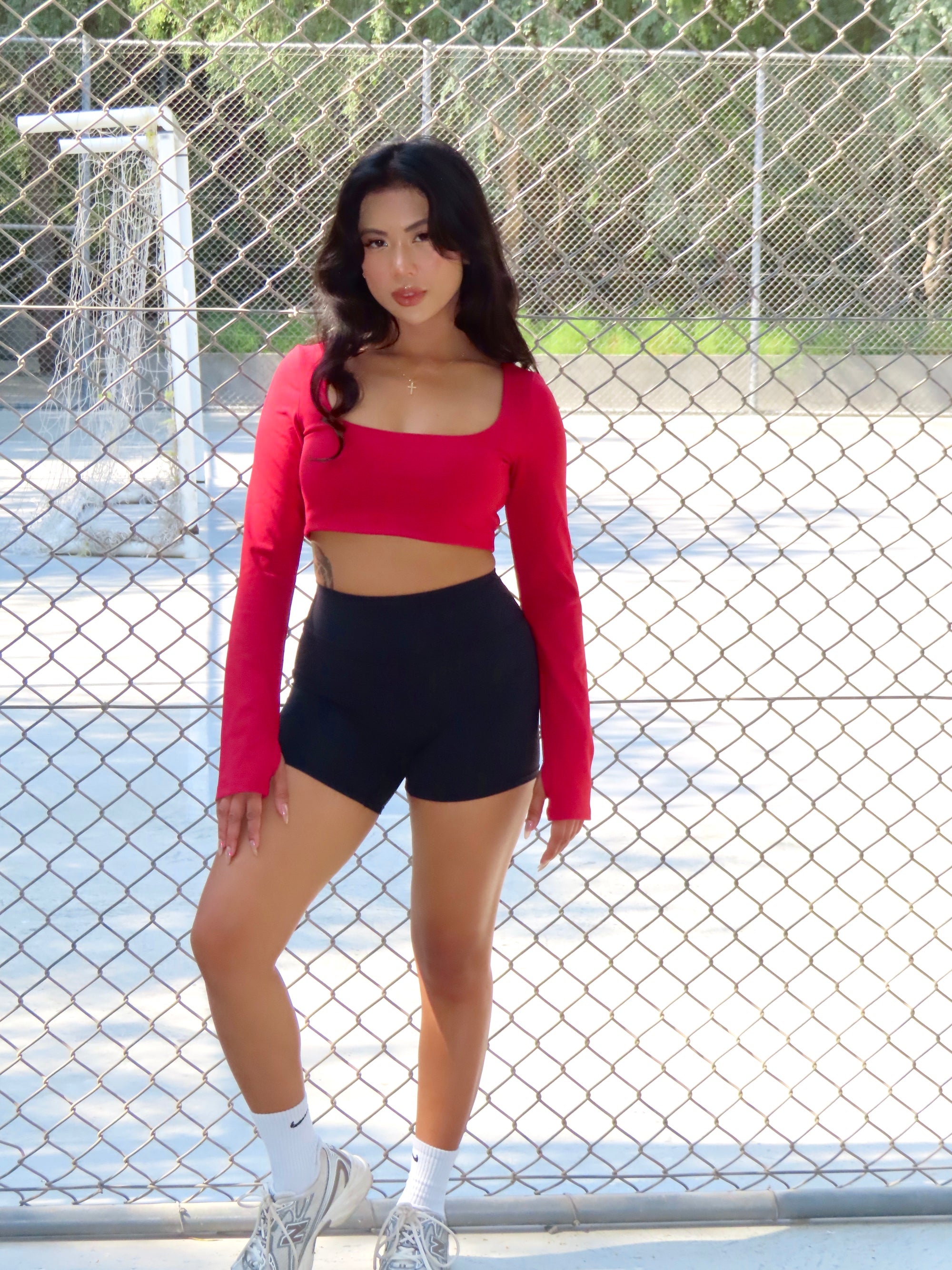Woman wearing the NAVA Fire Opal long-sleeve bra top outdoors, styled with black shorts for a sporty, casual look.