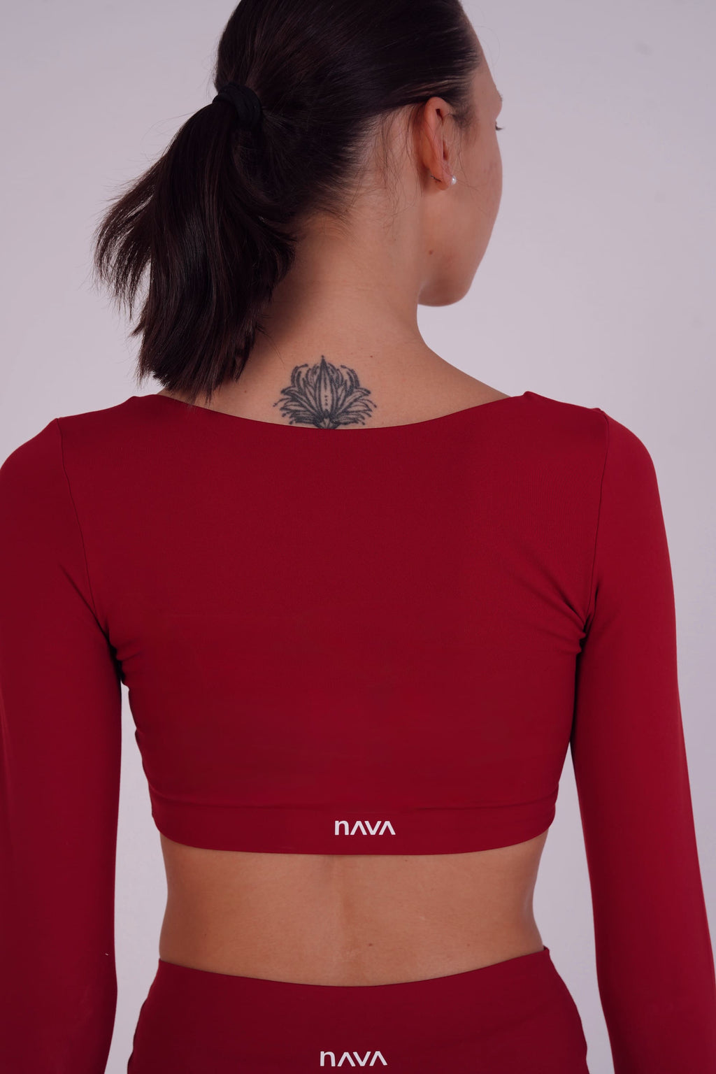 Person wearing a red long-sleeve crop top with 'NAVA' branding on a plain background