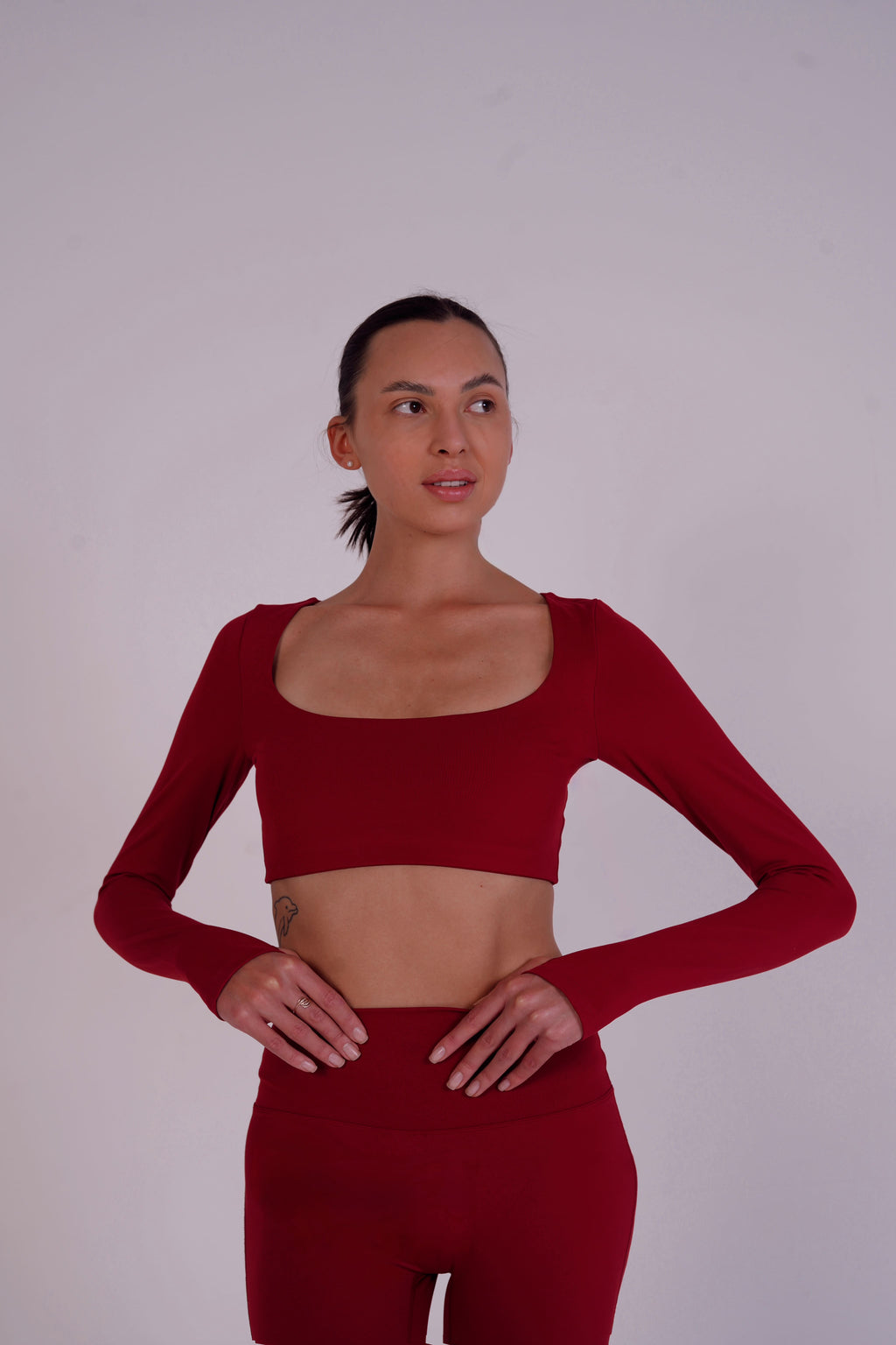 Woman wearing a red long-sleeve crop top and leggings against a plain background