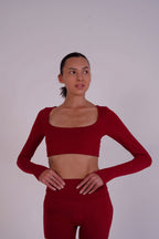Woman wearing a red long-sleeve crop top and leggings against a plain background
