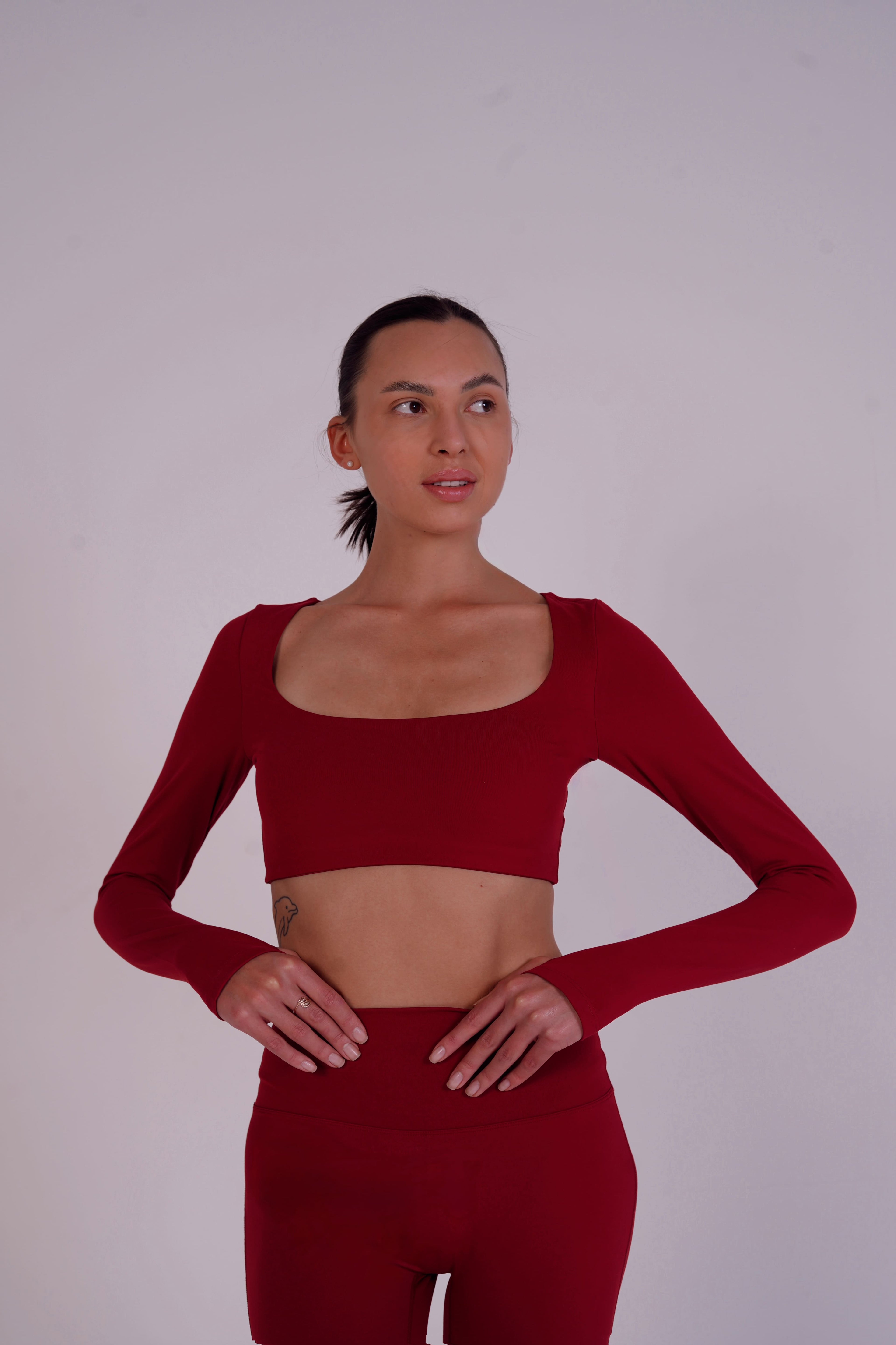 Woman wearing a red long-sleeve crop top and leggings against a plain background