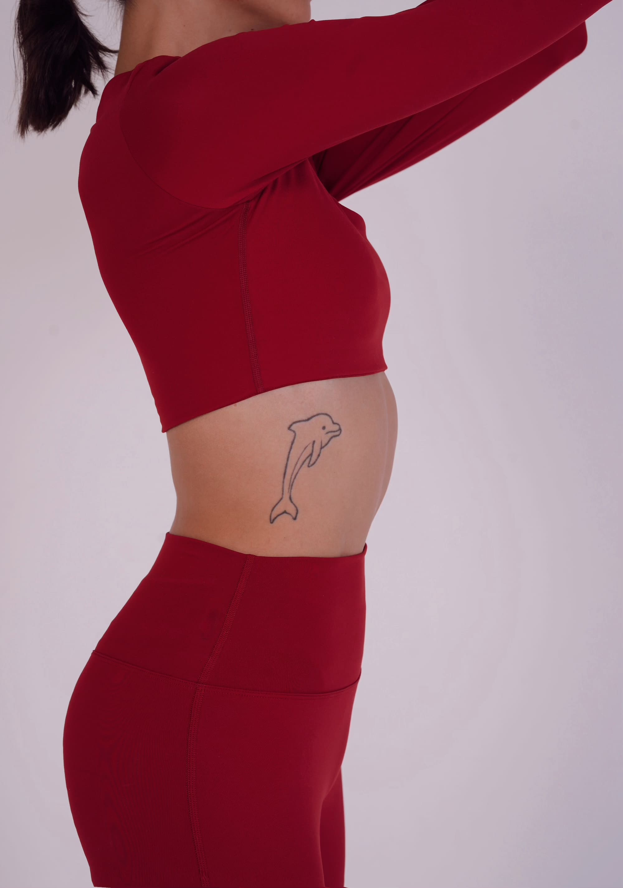 Person wearing a red athletic outfit with a dolphin tattoo on a plain background