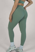 Person wearing green athletic leggings and sports bra on a plain background