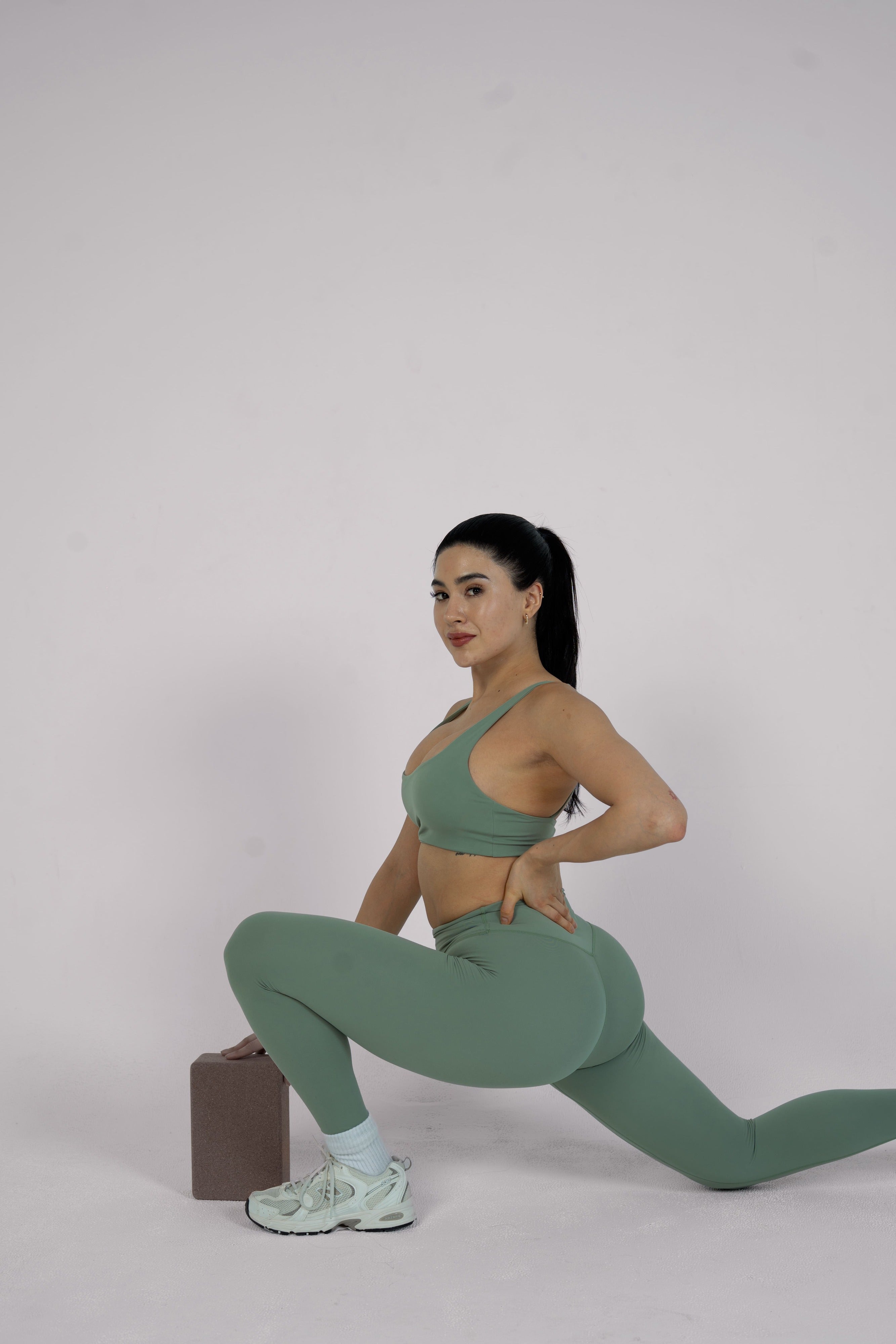 Woman in green athletic wear performing a lunge on a plain background
