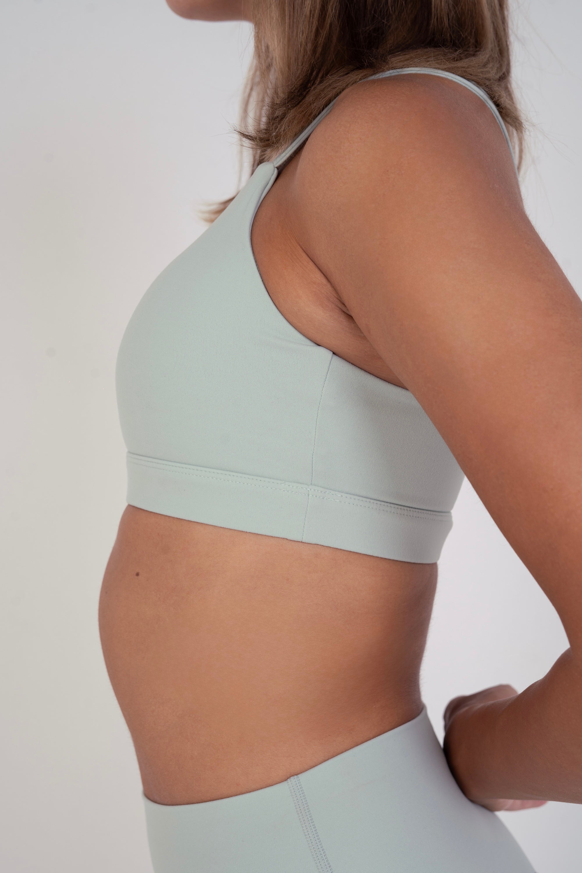 Side profile of NAVA Light Sage Green sports bra, showcasing smooth contour, wide band, and soft stretch fit.

