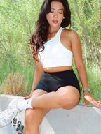 Woman in athletic wear sitting outdoors with greenery in the background