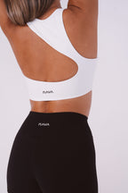 Person wearing a white sports bra and black leggings with 'Nava' branding on a light gray background