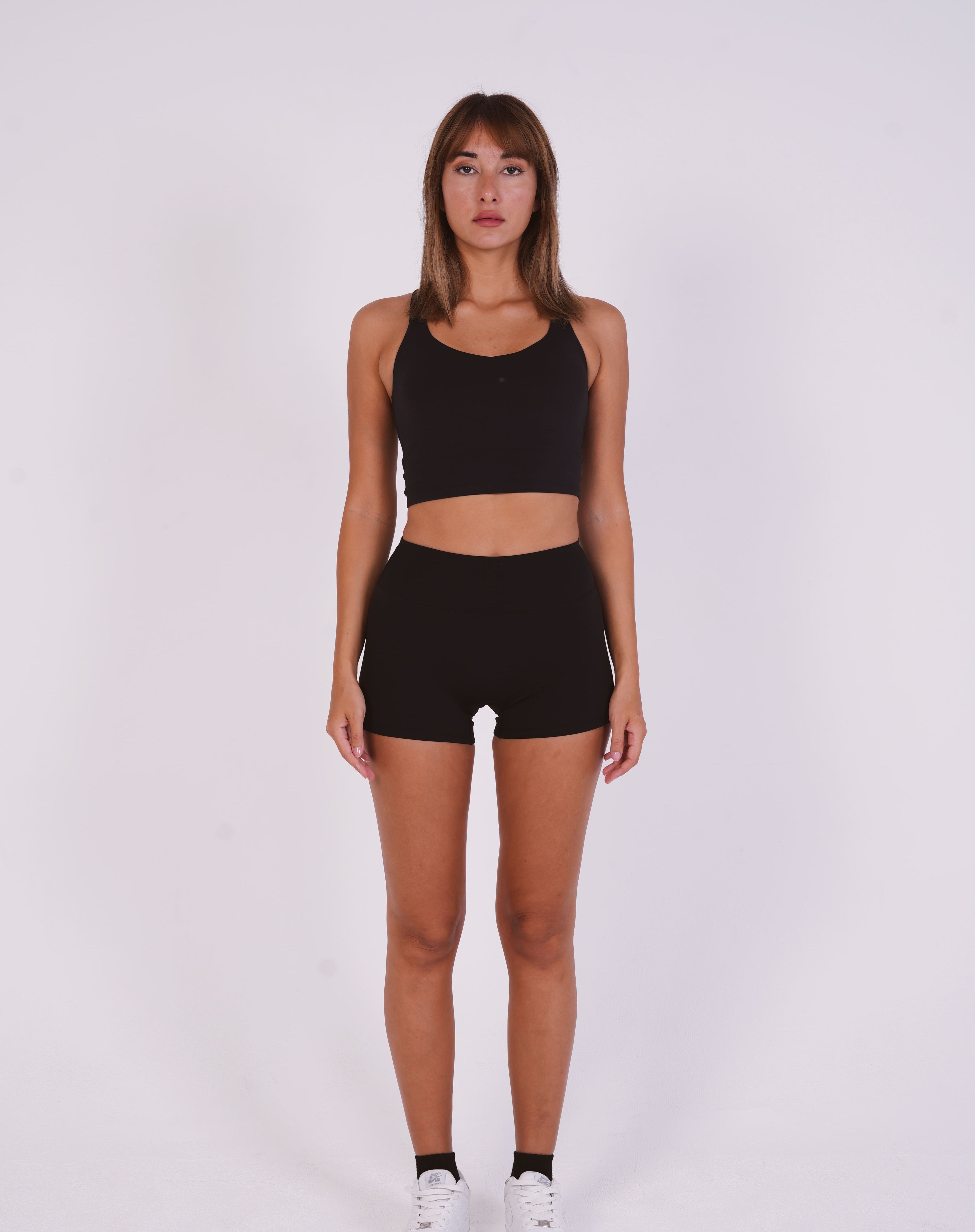 Woman wearing a black sports bra and shorts on a white background