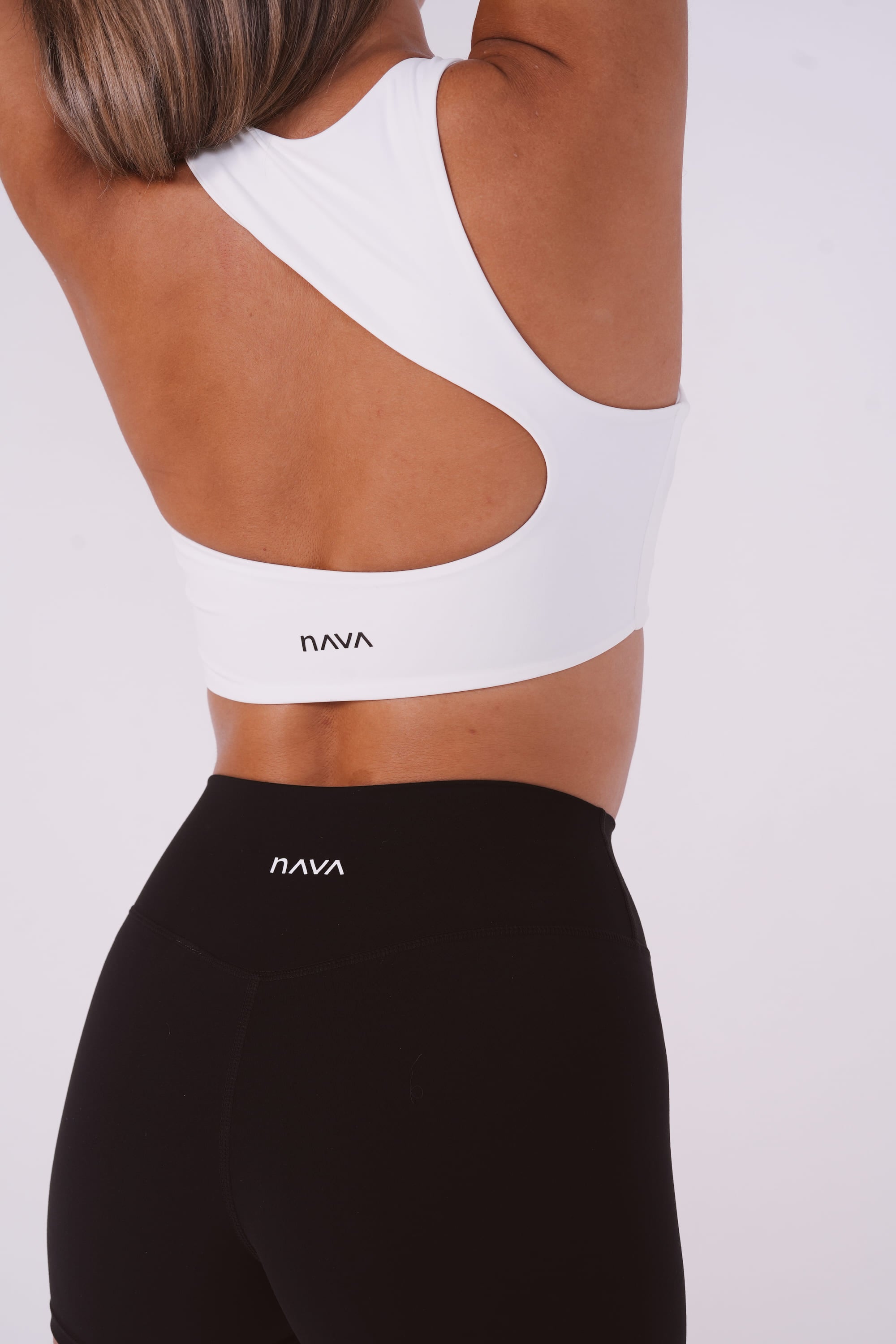 Person wearing a white sports bra and black leggings with 'Nava' branding on a light gray background