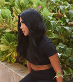 Woman in black outfit sitting among green foliage