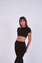 Woman wearing a black crop top and black pants on a white background