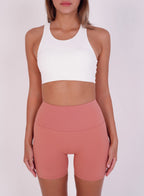 Person wearing a white sports bra and pink high-waisted shorts on a plain background