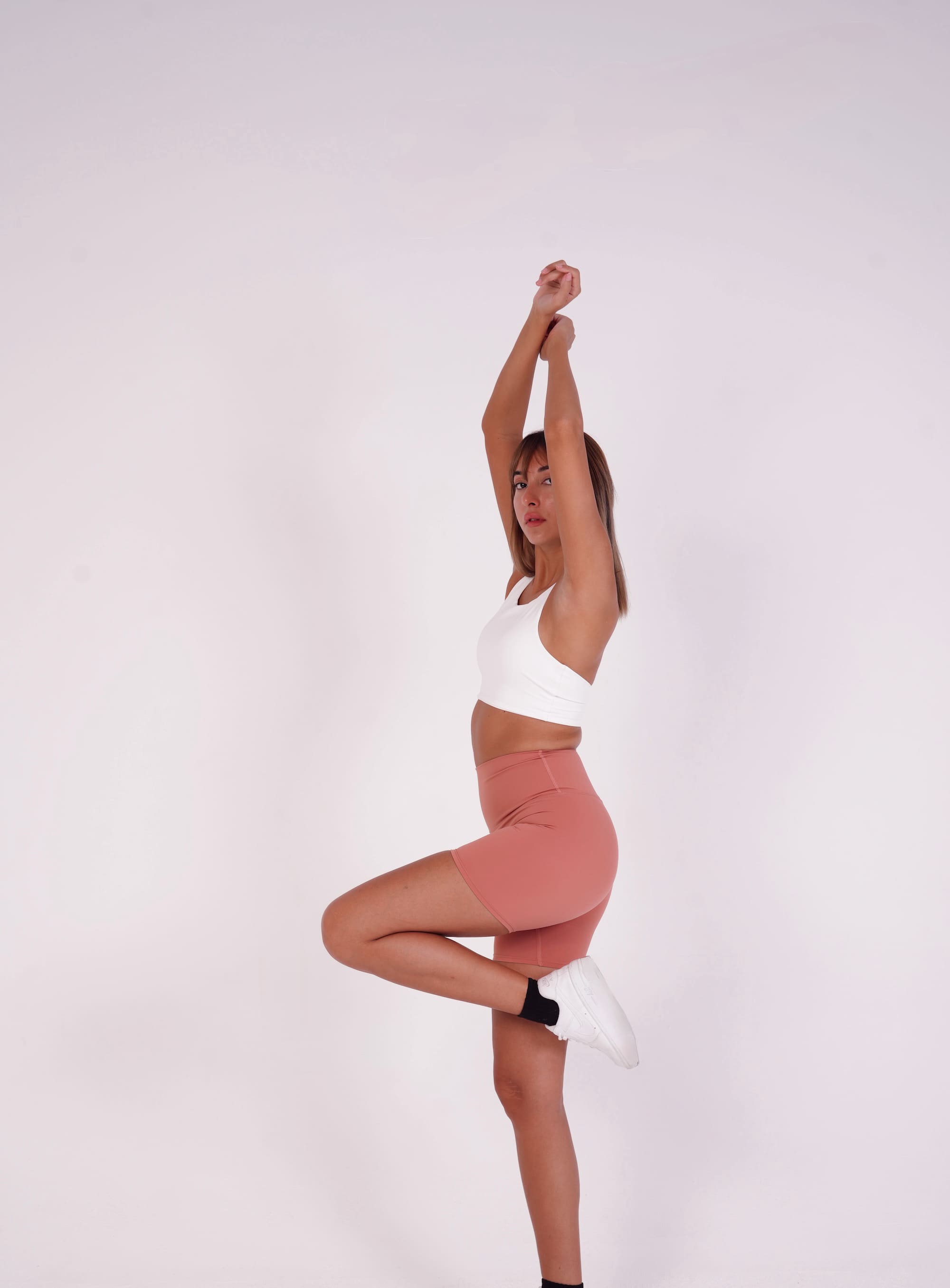 Person wearing a white sports bra and pink shorts on a light gray background