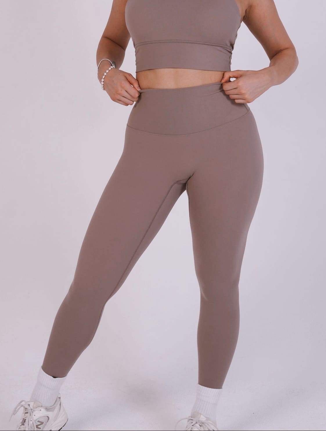 Person wearing brown athletic top and leggings on a white background