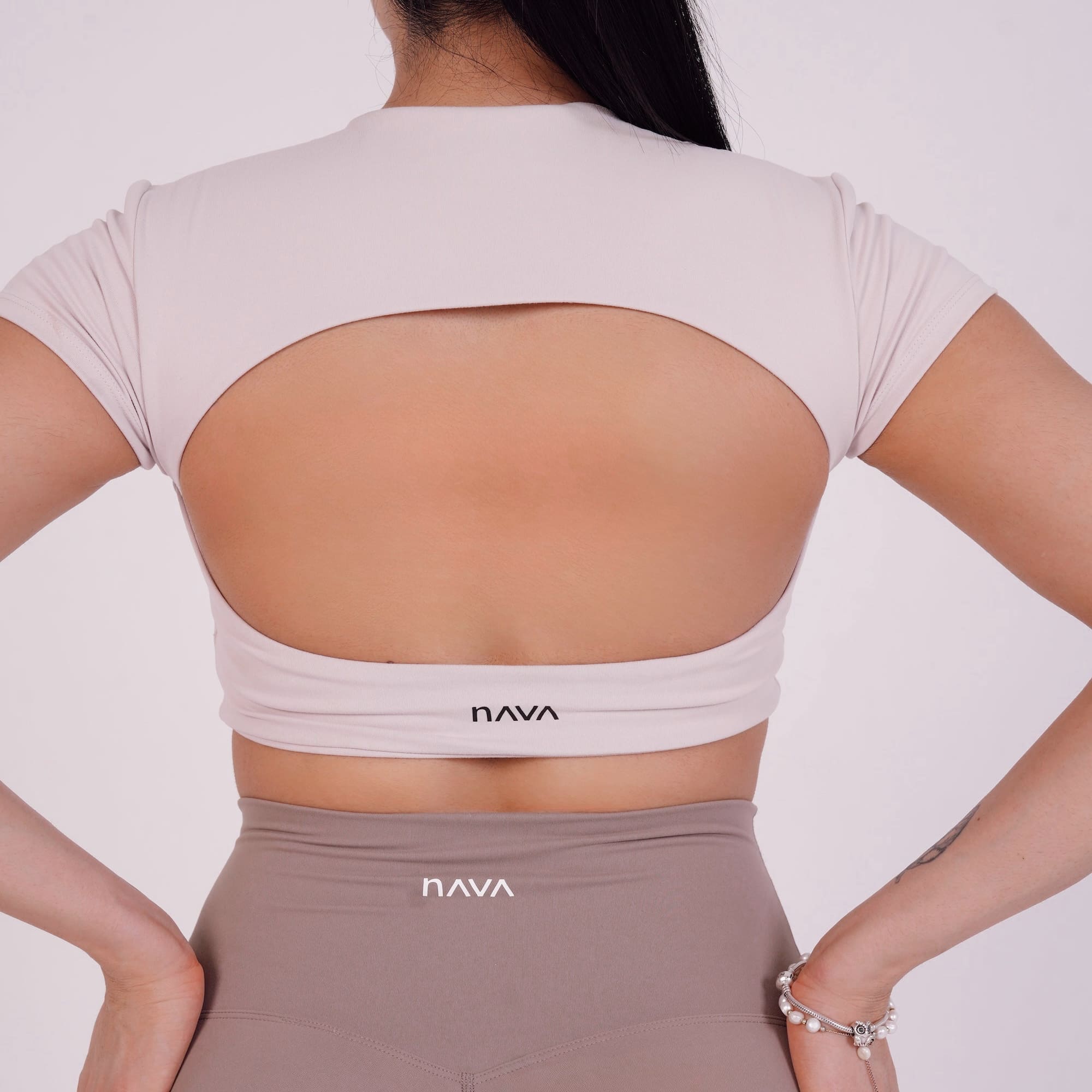 Person wearing a beige sports bra and leggings with 'NAVA' branding on a light gray background