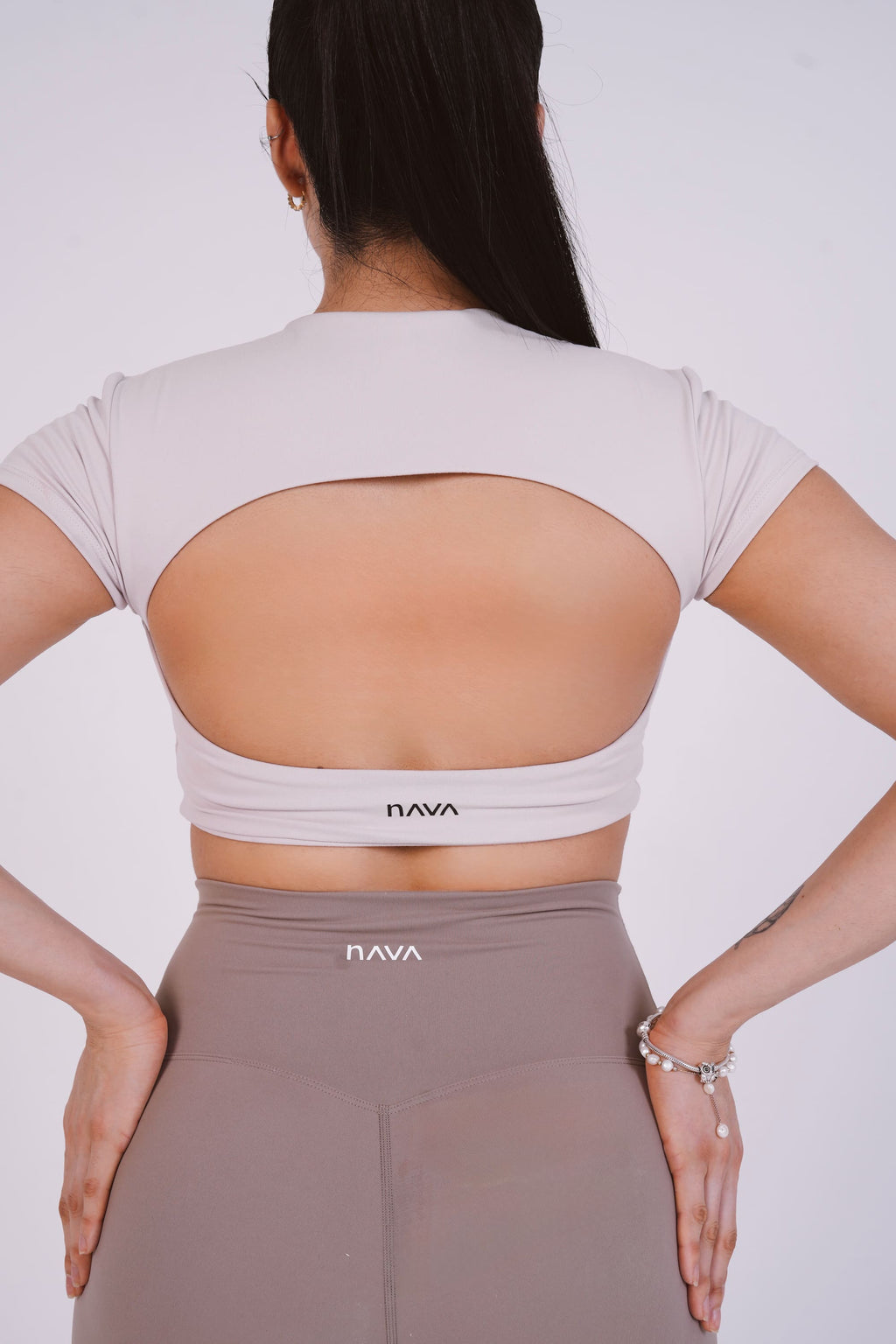 Woman wearing a beige open-back top and pants with 'Nava' branding on a white background
