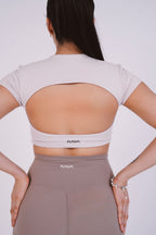 Woman wearing a beige open-back top and pants with 'Nava' branding on a white background
