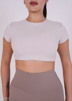 Person wearing a light gray crop top and brown high-waisted leggings on a white background