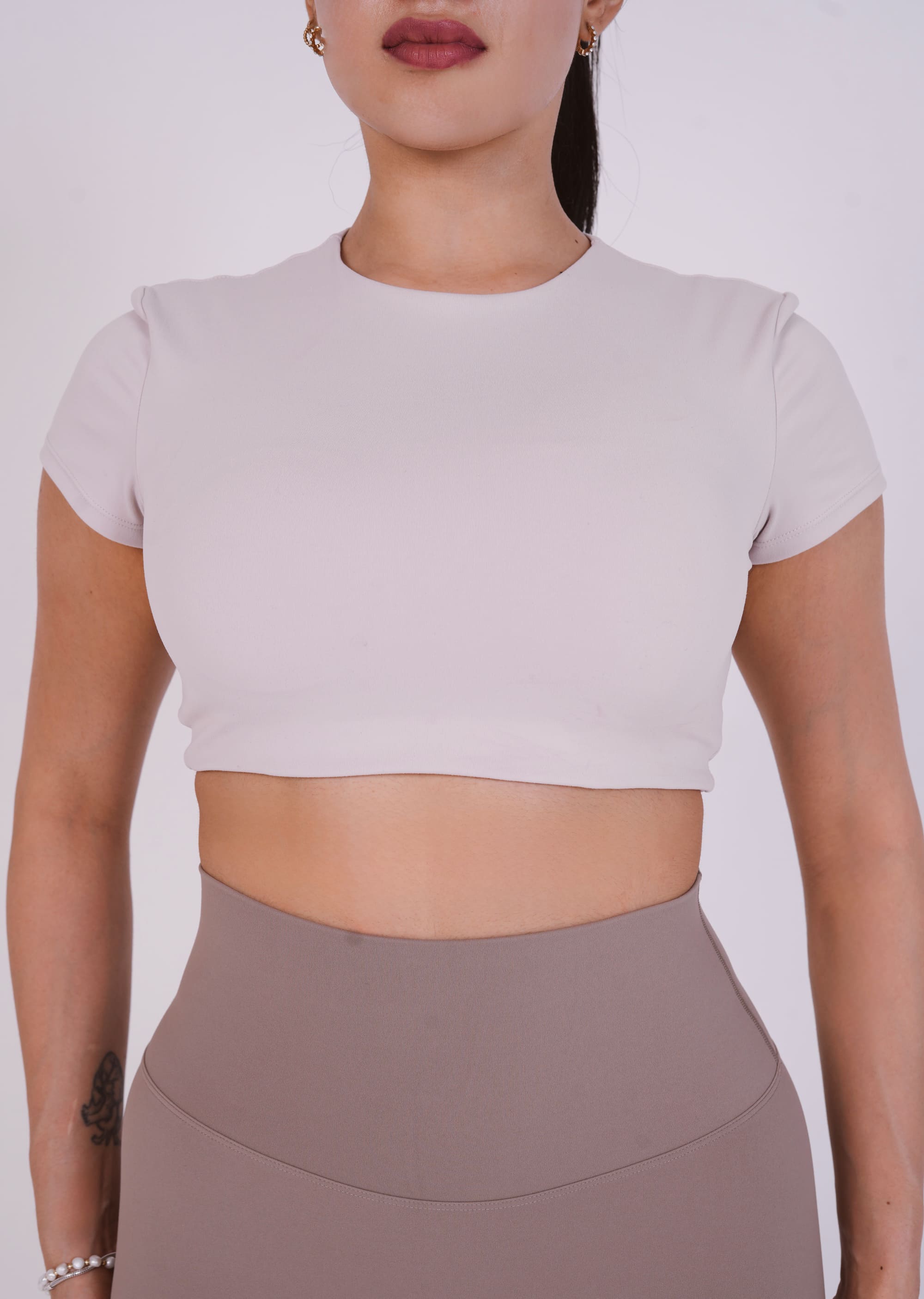 Person wearing a light gray crop top and brown high-waisted leggings on a white background