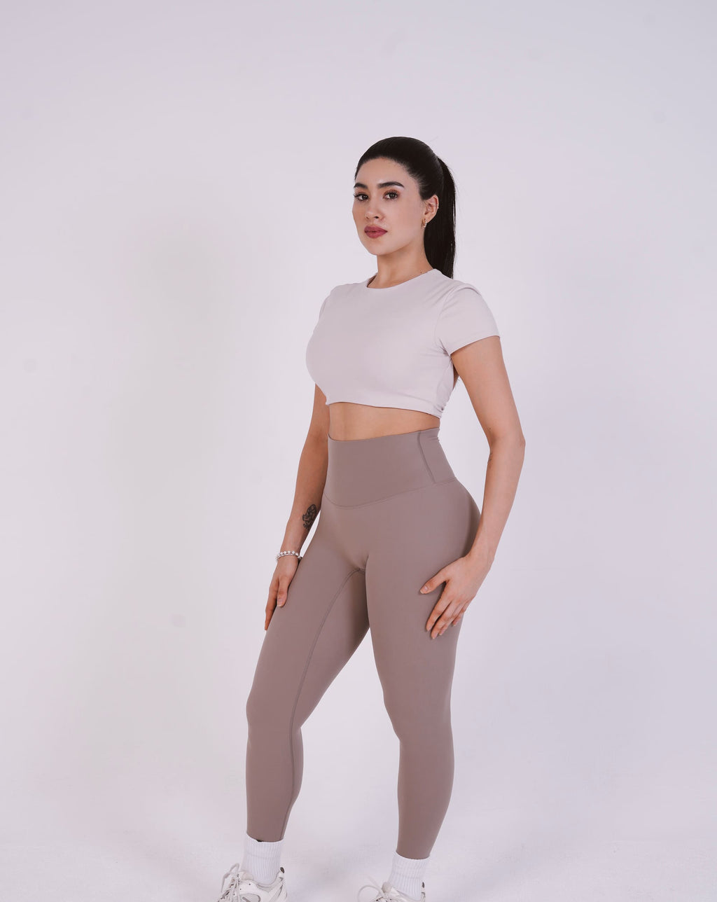 Woman wearing a light-colored crop top and high-waisted leggings on a white background