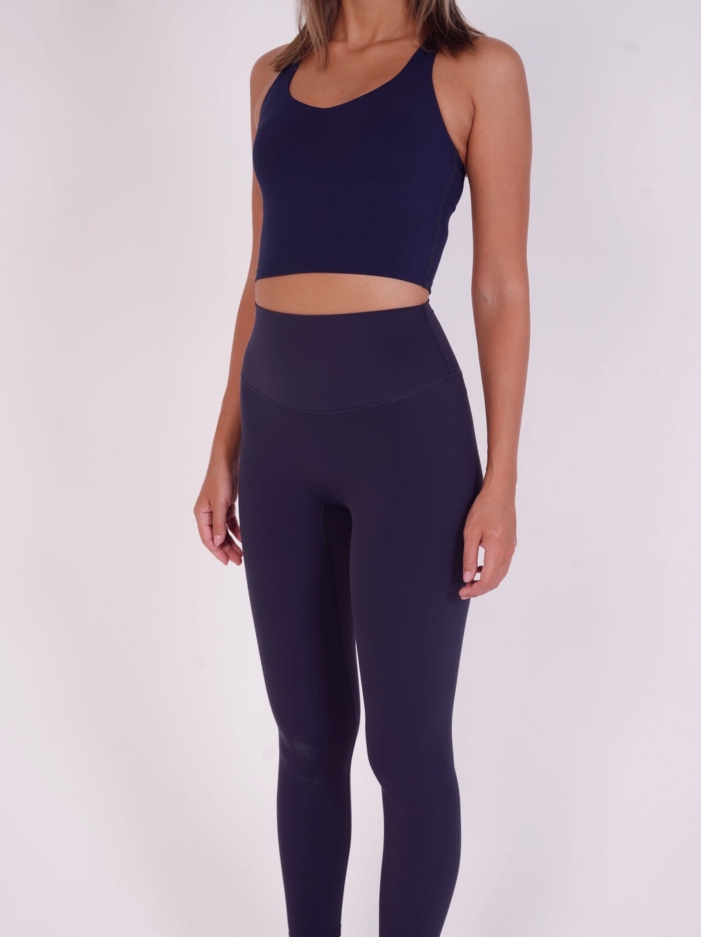 Person wearing a navy blue sports bra and leggings set on a white background